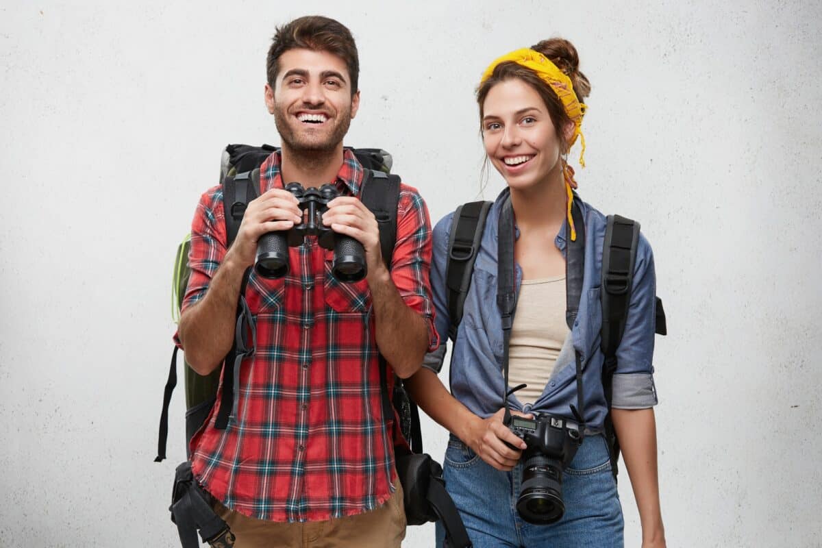 Couple caucasien joyeux, amoureux ou amis, équipé d'accessoires touristiques et de sacs à dos, prêt pour le voyage.