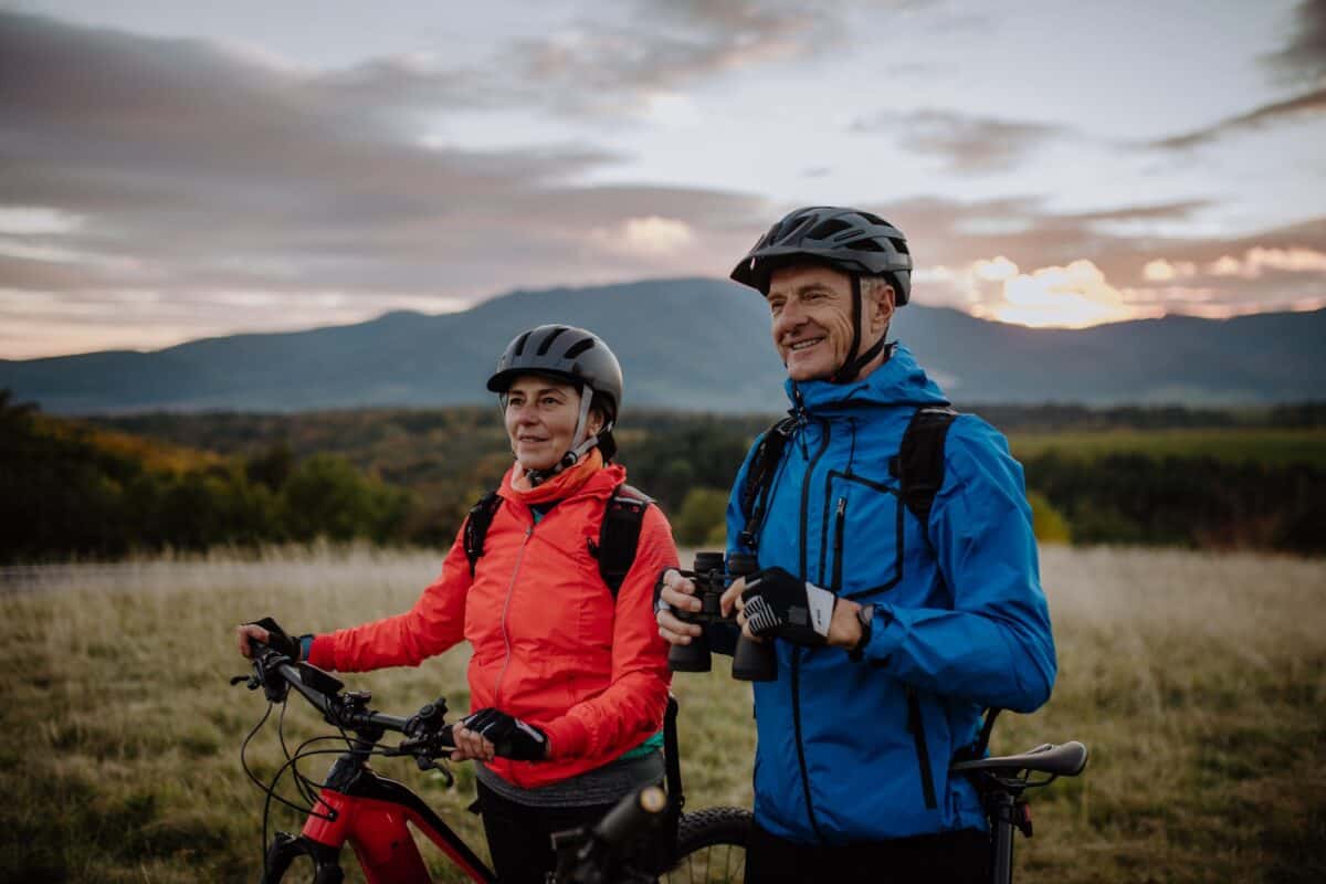Couple de seniors à vélo avec des jumelles admirant la nature en plein air dans une prairie en automne.